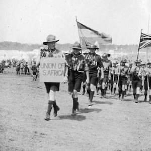 Scouts in uniforms marching with flags and a sign reading "Union of S. Africa"