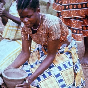 Image from the collection titled "Making Pottery at Kwilu" taken by Robert E. Smith in the 1960s.  It shows a woman kneeling over a clay bowl she is sculpting with her hands.