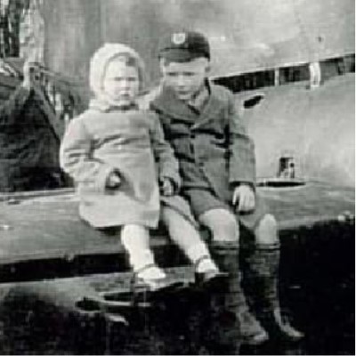 Childhood and Evacuation Detail of a photograph showing two children sitting on the wing of a crashed German fighter plane.