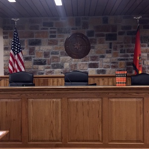 Image shows a judicial bench from the Cherokee Nation. Three chairs and two flags US and Cherokee are behind it.