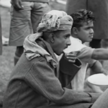 Video still showing a boy scout sitting and eating.  